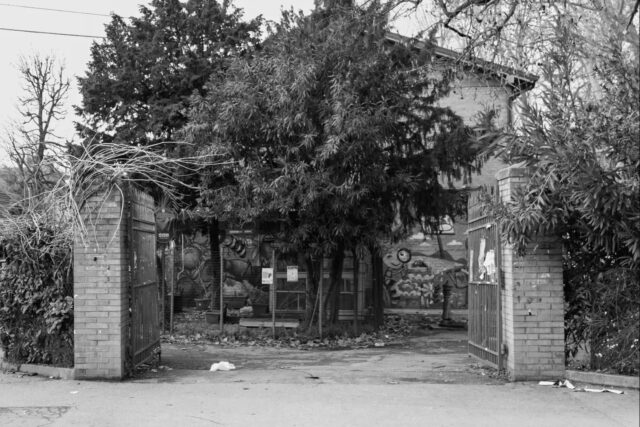 Cartoline dalla Bolognina – 2026
Il Fondo Comini

È un parco di quartiere come tanti: un ingresso su via Fioravanti, l'altro su via del Battiferro, i giochi, il campetto, le panchine. La storia interessante non è come è nato, ma chi lo tiene in piedi.

Per anni il nome girava male. Nelle cronache ci finiva per le aggressioni e per lo spaccio; nelle recensioni online era il parco "lasciato andare". Chi ci portava i bambini raccontava di alberi caduti e mai rimossi, giochi scrostati, e fra i rifiuti da terra vetri rotti, bottiglie, una volta perfino la lama di un coltello. Il posto dove si passa in fretta e non ci si ferma.

Eppure dentro il parco, dal 1997, c'è la Casa di Quartiere Fondo Comini, nata come centro sociale anziani e diventata negli anni un'altra cosa senza smettere di essere quella: ginnastica e ballo, ma anche doposcuola, italiano per donne straniere, teatro inclusivo, e le colazioni solidali con le Cucine Popolari, che qui al Battiferro hanno aperto la loro prima sede in città.

Nel 2021 alcune madri che frequentavano il parco hanno cominciato a pulirlo per conto proprio. Si sono date un nome, Spazza Comin, e una volta al mese raccolgono e ridipingono. Da lì è partita una trattativa lunga con il quartiere: aiuole, cancelli, un progetto portato al bilancio partecipativo.

Nel frattempo il parco si è riempito. D'estate ci sono le crescentine della domenica e Comini Espress, la rassegna che da giugno a settembre porta concerti e presentazioni. 

Nel maggio del 2025 ci si sono ritrovate diverse centinaia di persone per un'assemblea pubblica sul futuro del rione.

Il proprietario del parco non è mai cambiato: è pubblico. È cambiato chi ci passa il sabato mattina con la scopa.