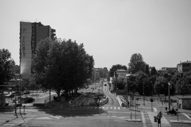 Cartoline dalla Bolognina – 2026
Fra via della Liberazione,Via Serlio e via Creti

Qui c'erano due fabbriche di macchine. Le Officine Minganti, torni e fresatrici per Fiat e Riv, chiudono a fine Novecento: nel 2006 riaprono come centro commerciale.

Le Officine Cevolani, macchine per il confezionamento in un capannone costruito apposta nel 1940, passano a Pelliconi nel 1999 e lasciano la Bolognina. Il capannone resta vuoto quattordici anni, e chi abita qui sa cosa ci si fermava dentro. Viene abbattuto nel 2013.

Al suo posto la P-Tower: autorizzata nel 2011, ferma per la crisi, in cantiere dal 2016, quattordici piani. Poi le P-House, 150 appartamenti con piscina sul tetto. 

Poco lontano, in via Serlio, uno studentato di sedici piani: 513 miniappartamenti da 900 a 1.240 euro al mese, contestato dai residenti per l'ombra sulle case.

Un rione nato operaio, che ha visto le fabbriche chiudere e marcire, e che oggi ospita chi fino a fine anni Novanta non avrebbe messo piede in queste vie.